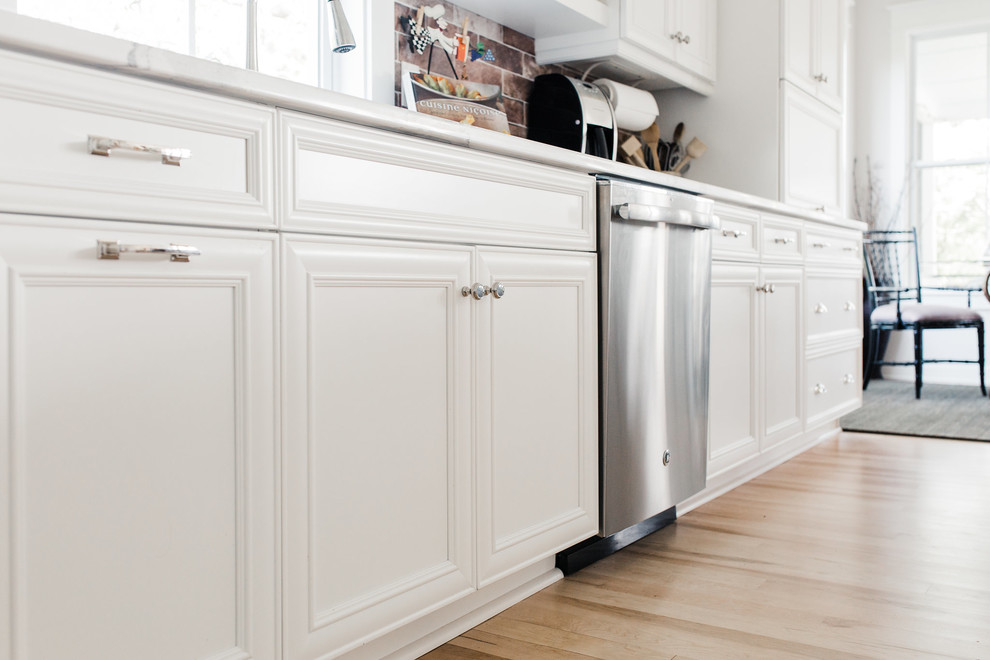 Foto på ett mellanstort vintage vit kök, med vita skåp, stänkskydd i tegel, en köksö, en undermonterad diskho, skåp i shakerstil, bänkskiva i kvarts, rött stänkskydd, rostfria vitvaror, ljust trägolv och beiget golv