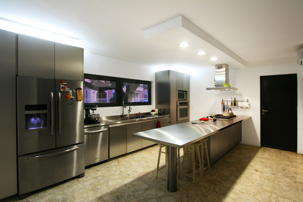 Photo of a contemporary kitchen/diner in Other with an integrated sink, flat-panel cabinets, stainless steel cabinets, stainless steel worktops, stainless steel appliances, terrazzo flooring and a breakfast bar.