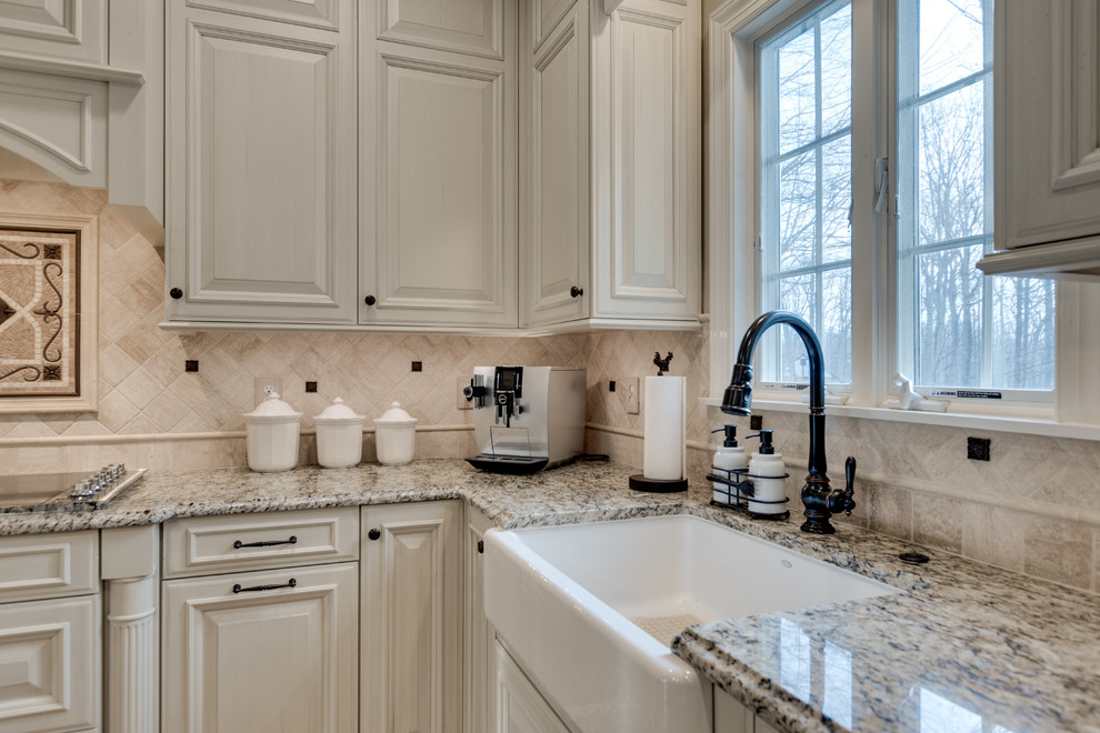 This is an example of a large classic kitchen in Baltimore with a belfast sink, raised-panel cabinets, granite worktops, beige splashback, travertine splashback, stainless steel appliances, light hardwood flooring and an island.