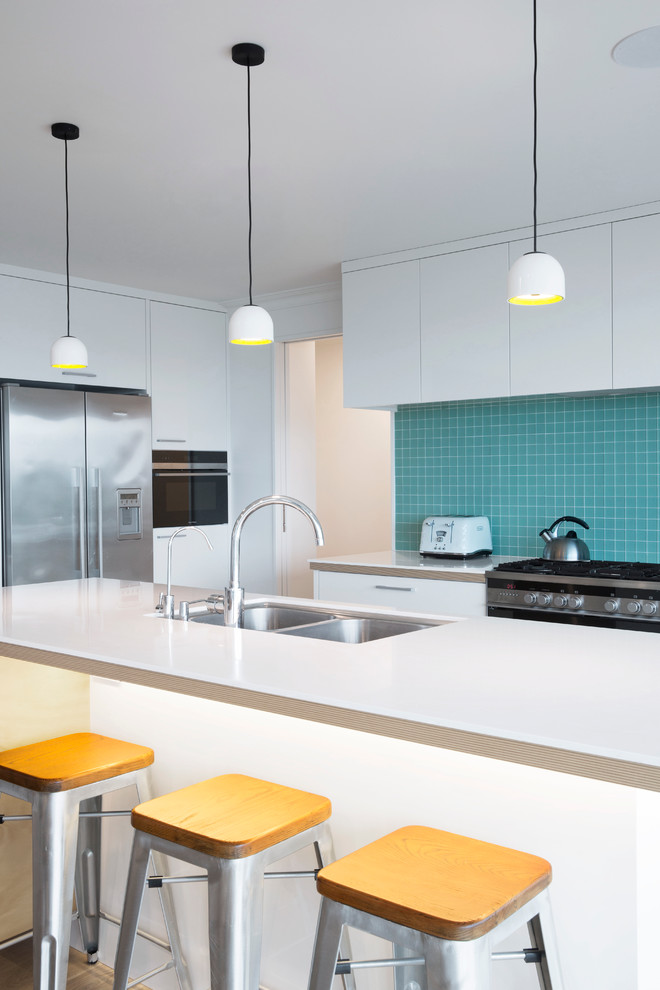 Bild på ett mellanstort minimalistiskt kök, med en dubbel diskho, släta luckor, vita skåp, blått stänkskydd, stänkskydd i mosaik, rostfria vitvaror, ljust trägolv och en köksö