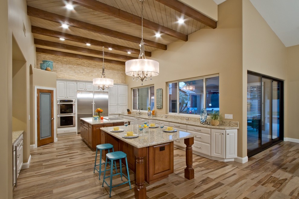 Example of a large eclectic galley light wood floor and brown floor eat-in kitchen design in Phoenix with a drop-in sink, beaded inset cabinets, white cabinets, granite countertops, beige backsplash, stainless steel appliances and two islands