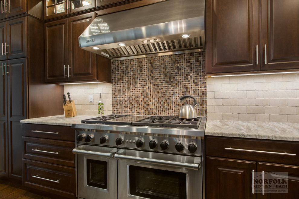 Klassisk inredning av ett kök, med en rustik diskho, skåp i mörkt trä, granitbänkskiva, beige stänkskydd, rostfria vitvaror, mellanmörkt trägolv och en köksö