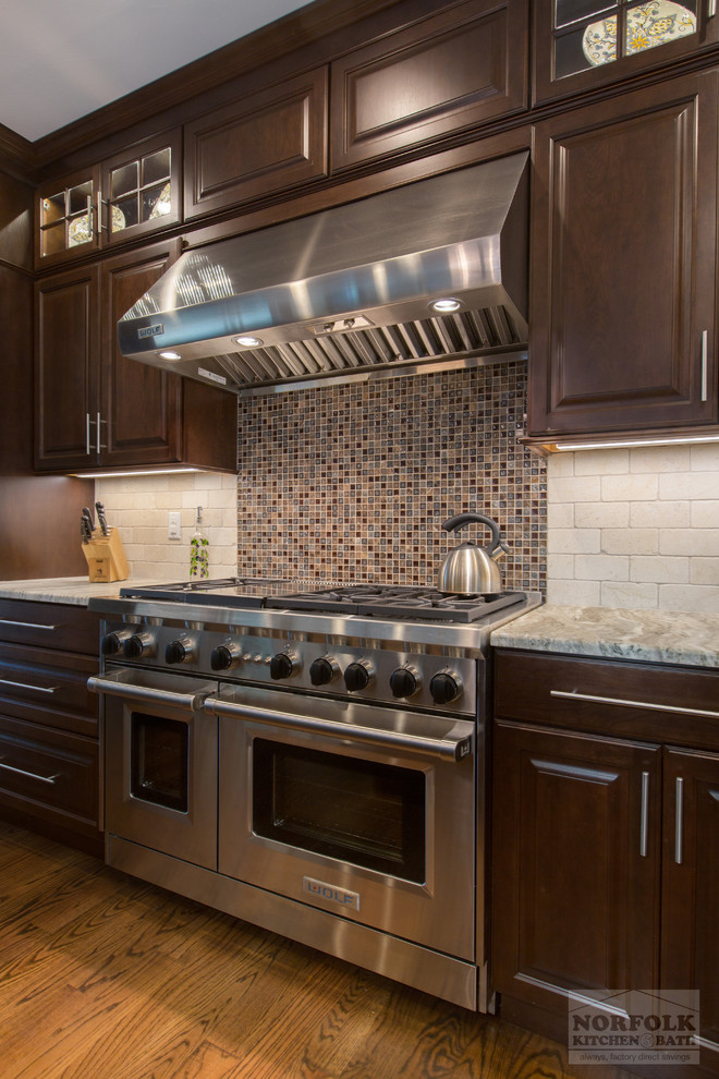 Klassische Küche mit Landhausspüle, dunklen Holzschränken, Granit-Arbeitsplatte, Küchenrückwand in Beige, Küchengeräten aus Edelstahl, braunem Holzboden und Kücheninsel in Boston