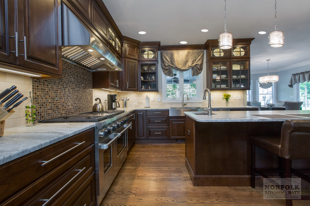 Inspiration for a transitional medium tone wood floor kitchen remodel in Boston with a farmhouse sink, dark wood cabinets, granite countertops, beige backsplash, stainless steel appliances and an island