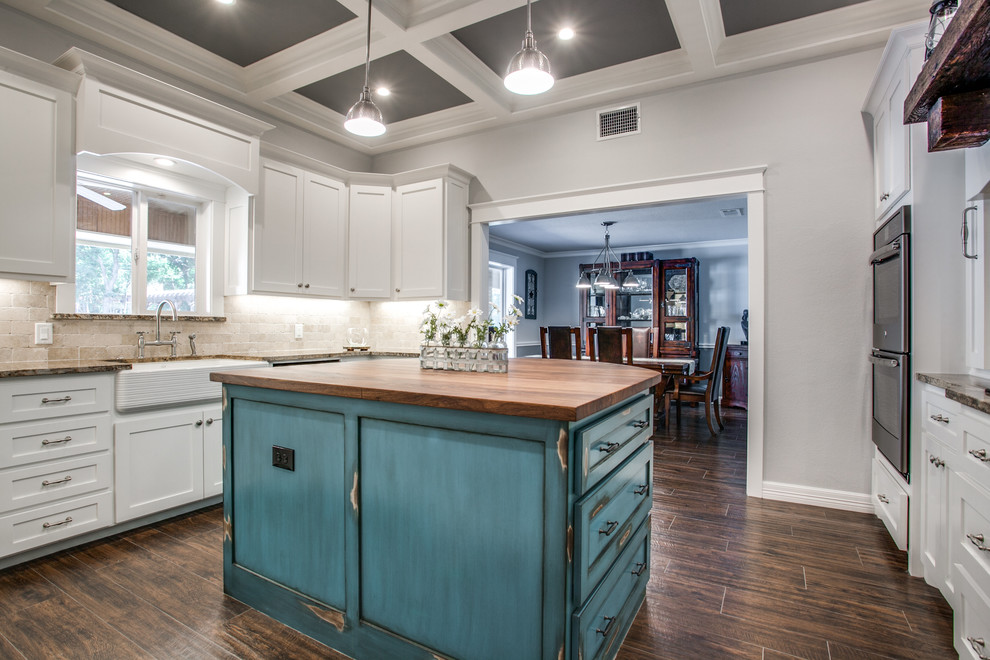 Enclosed kitchen - mid-sized farmhouse u-shaped medium tone wood floor and brown floor enclosed kitchen idea in Dallas with a farmhouse sink, shaker cabinets, white cabinets, granite countertops, beige backsplash, stone tile backsplash, stainless steel appliances and an island