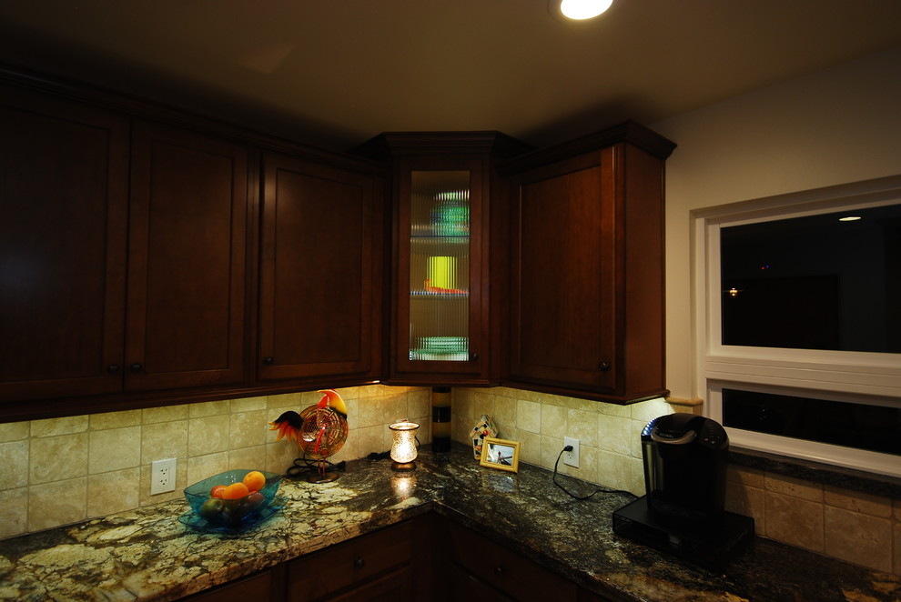Klassisk inredning av ett mellanstort kök, med en undermonterad diskho, luckor med infälld panel, skåp i mellenmörkt trä, granitbänkskiva, beige stänkskydd, stänkskydd i stenkakel, rostfria vitvaror och klinkergolv i porslin