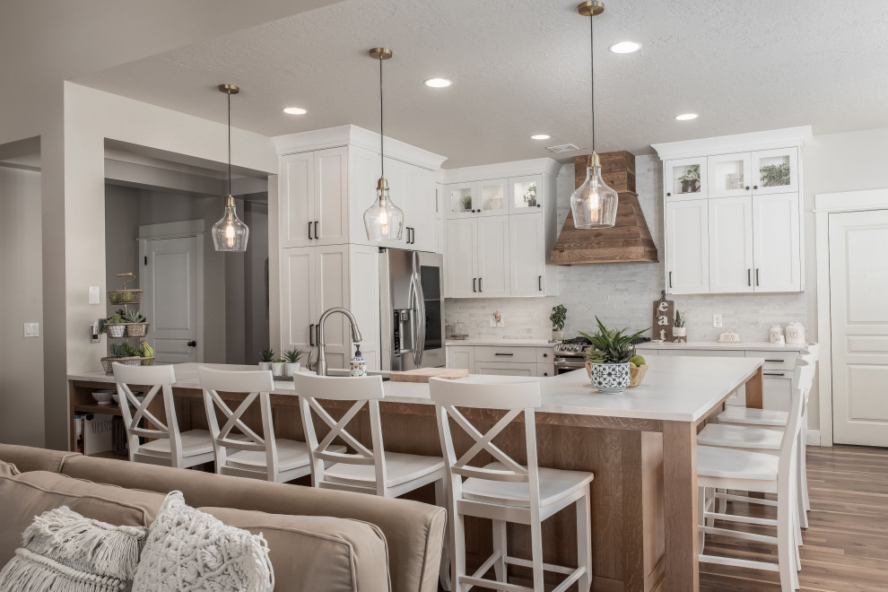 Mid-sized country l-shaped medium tone wood floor eat-in kitchen photo in Salt Lake City with a drop-in sink, shaker cabinets, white cabinets, quartz countertops, white backsplash, stone tile backsplash, stainless steel appliances, an island and white countertops