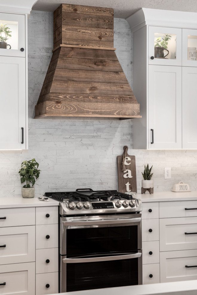 Bild på ett mellanstort lantligt vit vitt kök, med en nedsänkt diskho, skåp i shakerstil, vita skåp, bänkskiva i kvarts, vitt stänkskydd, stänkskydd i stenkakel, rostfria vitvaror, mellanmörkt trägolv och en köksö