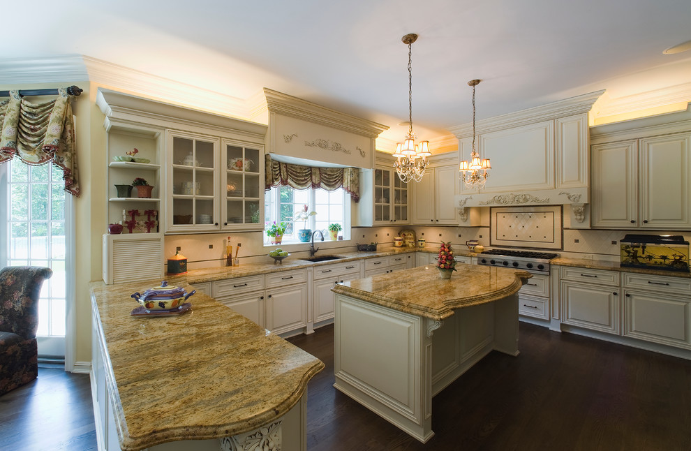 Klassisk inredning av ett kök, med granitbänkskiva, en undermonterad diskho, luckor med upphöjd panel, beige skåp, beige stänkskydd, stänkskydd i keramik, rostfria vitvaror, mörkt trägolv och en köksö