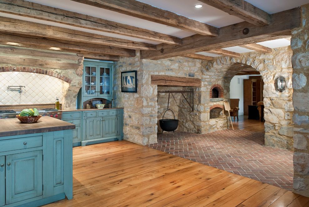 Example of a mountain style l-shaped brick floor eat-in kitchen design in Philadelphia with stainless steel appliances, raised-panel cabinets, blue cabinets, wood countertops, white backsplash, an undermount sink, porcelain backsplash and an island