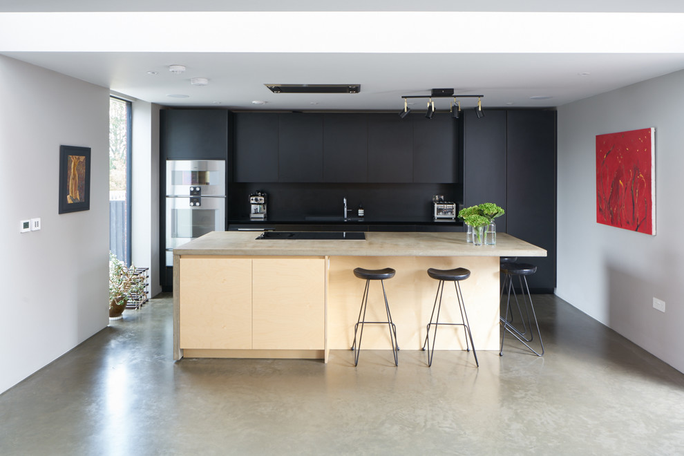 Large modern open plan kitchen in London with an integrated sink, flat-panel cabinets, black cabinets, concrete worktops, black splashback, integrated appliances, concrete flooring and an island.