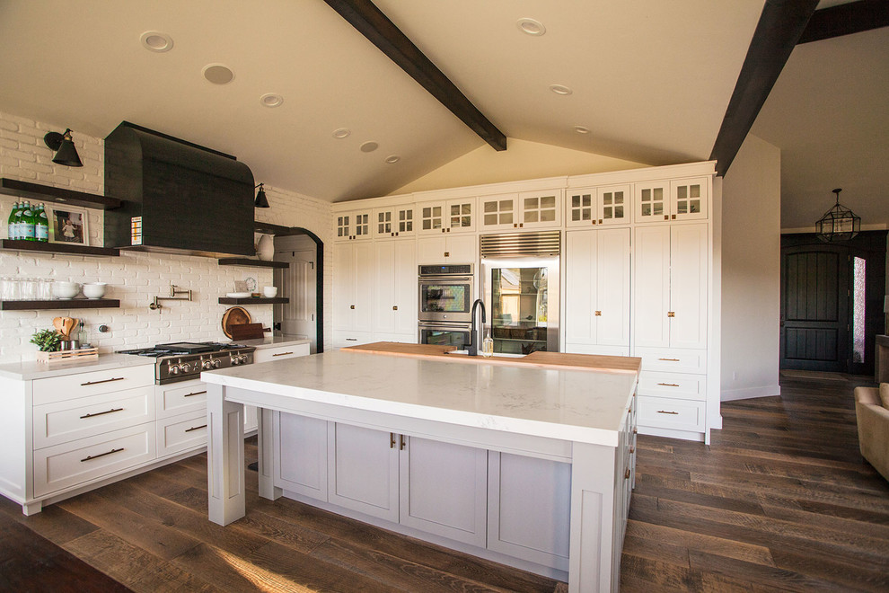 Inspiration for a mid-sized transitional l-shaped medium tone wood floor open concept kitchen remodel in Salt Lake City with a farmhouse sink, shaker cabinets, white cabinets, white backsplash, stainless steel appliances, an island and quartzite countertops
