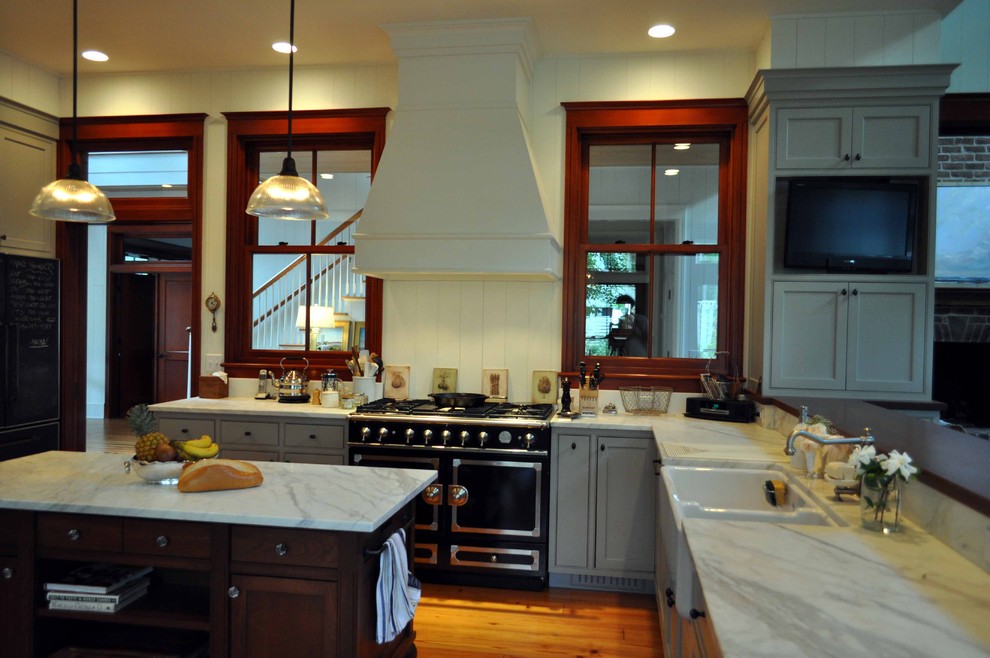 Klassisk inredning av ett stort kök, med en rustik diskho, skåp i shakerstil, grå skåp, svarta vitvaror, marmorbänkskiva, vitt stänkskydd och mörkt trägolv