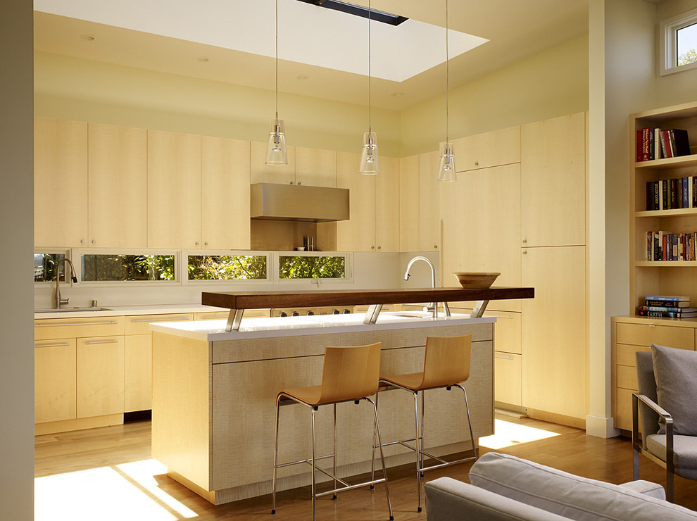 На фото: угловая кухня-гостиная в стиле модернизм с плоскими фасадами, светлыми деревянными фасадами и барной стойкой
