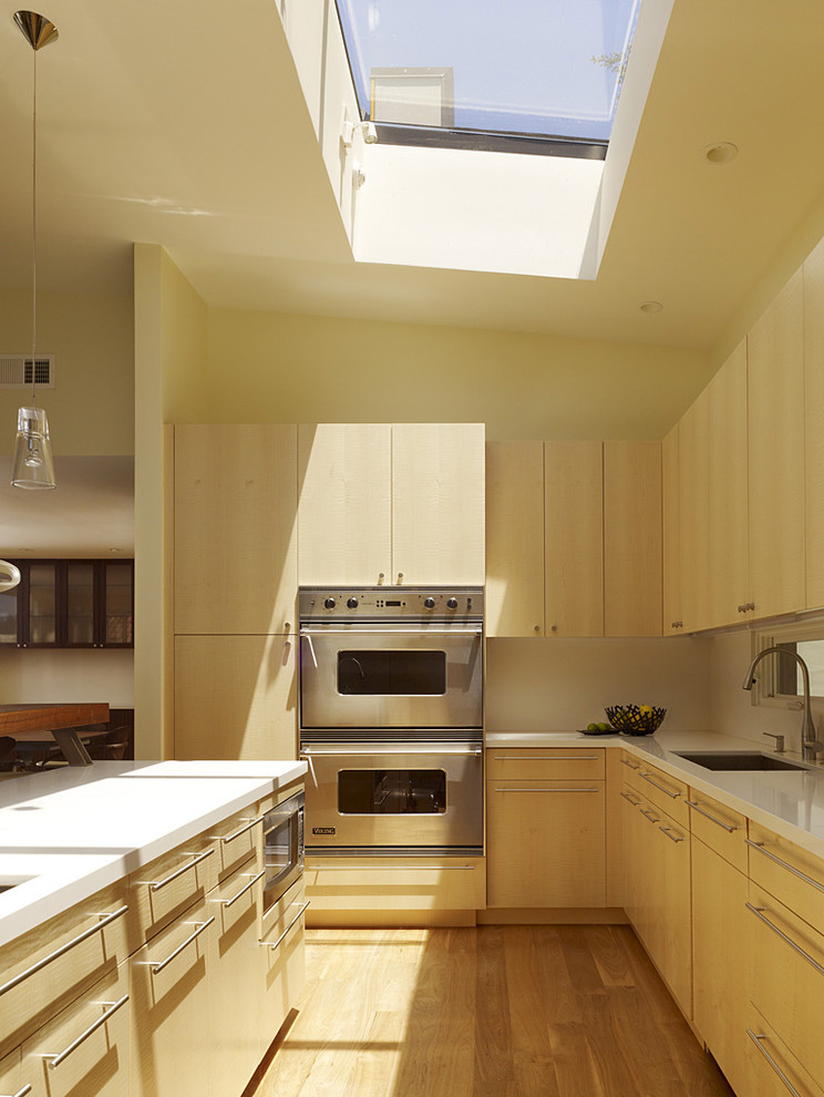 Immagine di una cucina moderna con elettrodomestici in acciaio inossidabile, lavello sottopiano, ante lisce e ante in legno chiaro