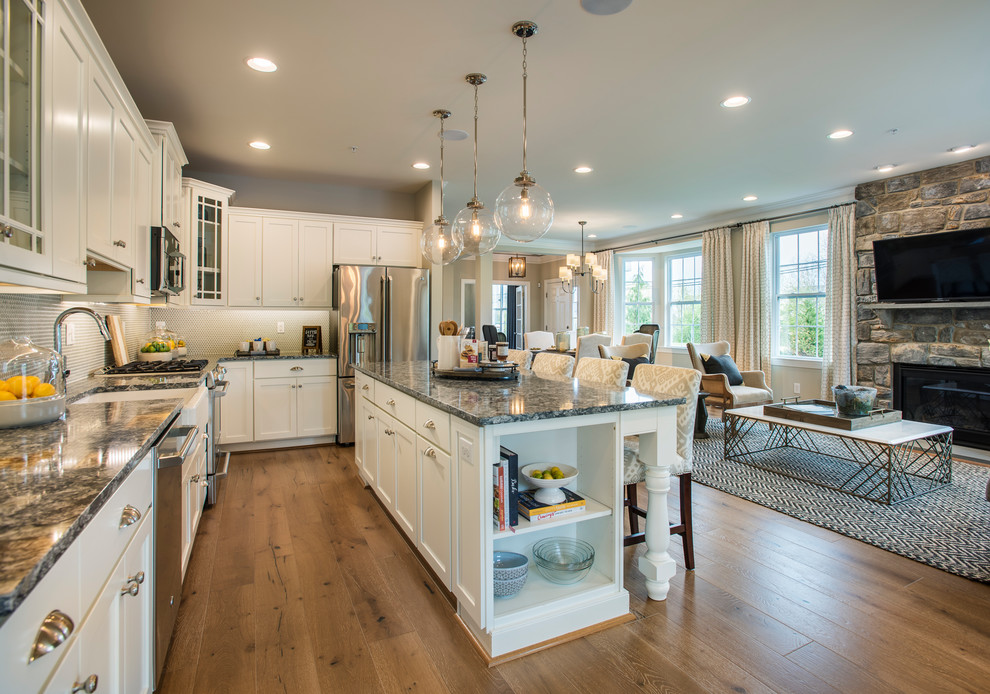 Example of a mid-sized transitional l-shaped light wood floor open concept kitchen design in Philadelphia with a farmhouse sink, recessed-panel cabinets, white cabinets, quartz countertops, gray backsplash, stainless steel appliances and an island