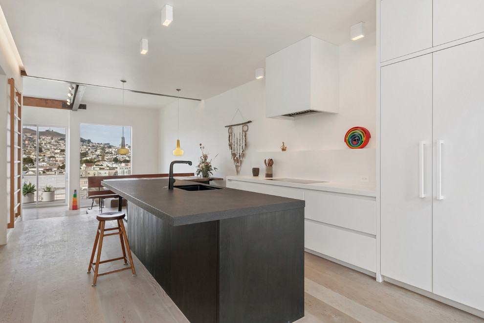 Large scandinavian galley kitchen pantry in San Francisco with an integrated sink, flat-panel cabinets, white cabinets, granite worktops, white appliances, light hardwood flooring and an island.
