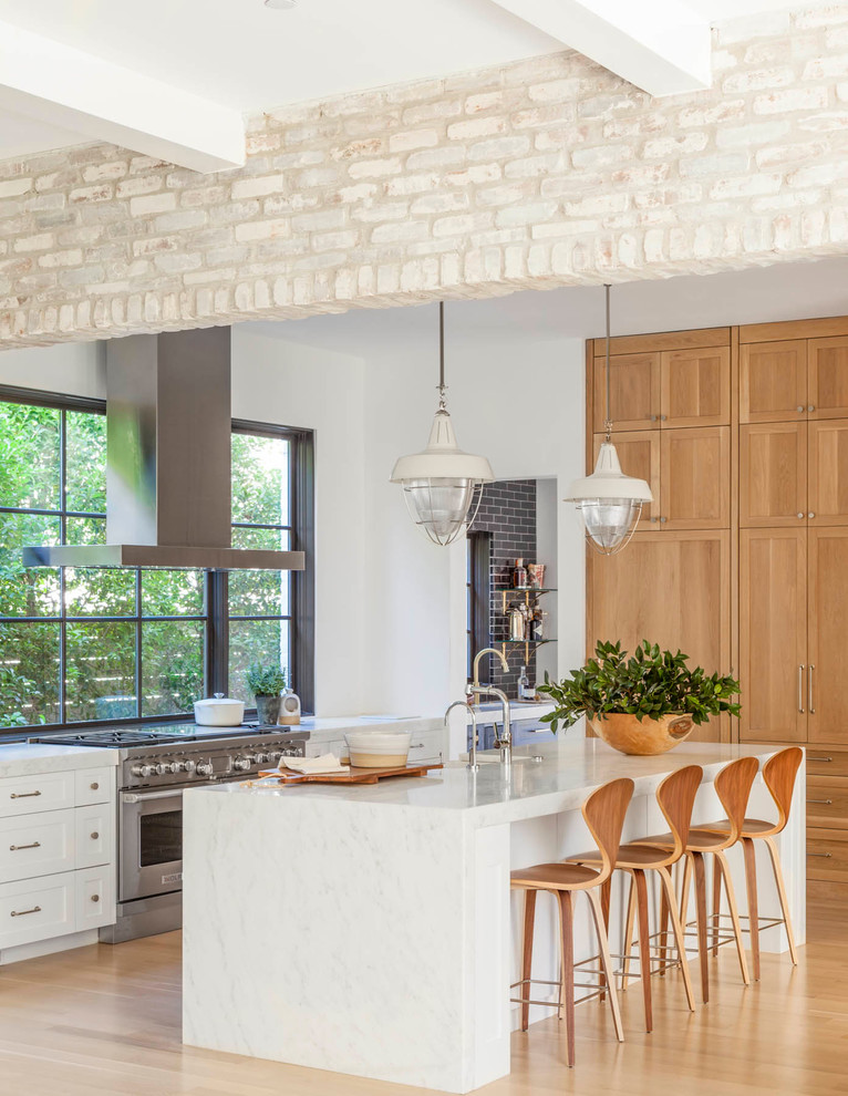 Inredning av ett klassiskt stort grå grått kök, med skåp i shakerstil, skåp i ljust trä, rostfria vitvaror, ljust trägolv, en köksö, en rustik diskho, marmorbänkskiva, fönster som stänkskydd och brunt golv