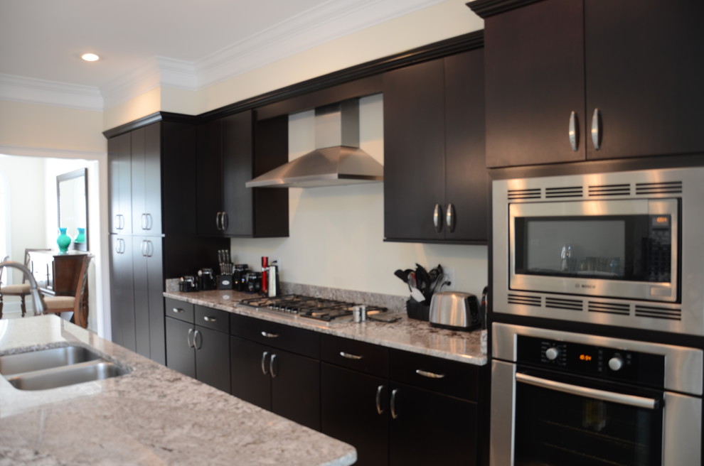 Example of a classic galley kitchen design in Other with an undermount sink, flat-panel cabinets, dark wood cabinets, granite countertops, beige backsplash and stainless steel appliances