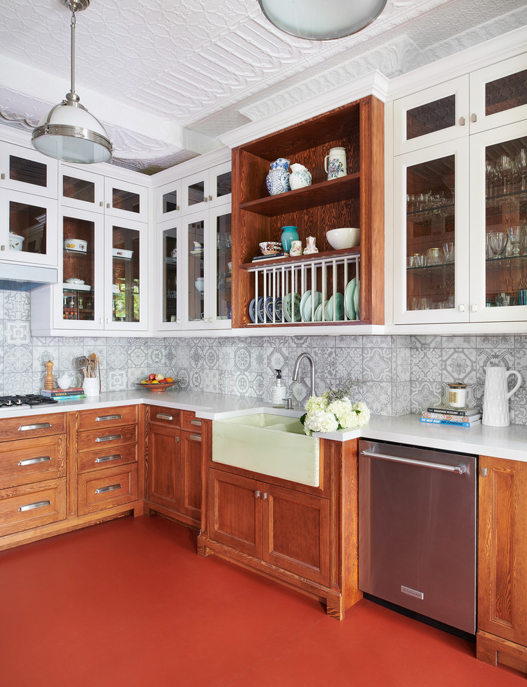 Example of a mid-sized eclectic u-shaped concrete floor and red floor enclosed kitchen design in Toronto with a farmhouse sink, shaker cabinets, medium tone wood cabinets, solid surface countertops, gray backsplash, ceramic backsplash, stainless steel appliances, no island and white countertops