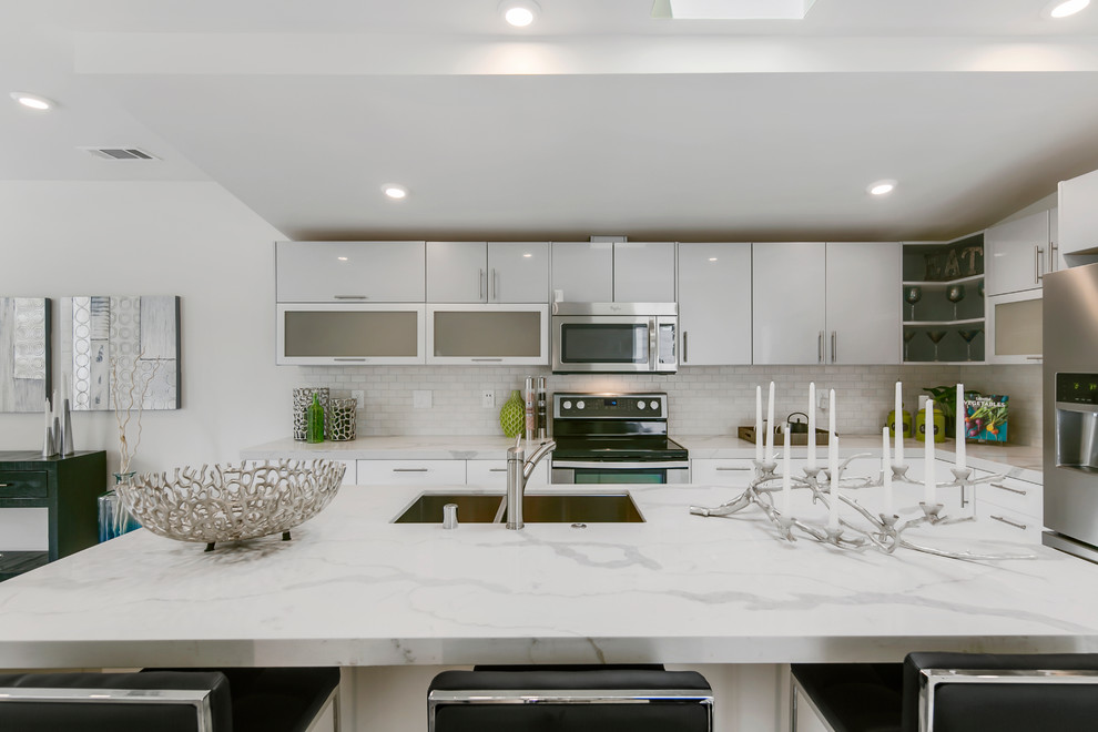 This is an example of a medium sized modern l-shaped open plan kitchen in San Francisco with a double-bowl sink, flat-panel cabinets, white cabinets, marble worktops, white splashback, ceramic splashback, stainless steel appliances, an island and laminate floors.