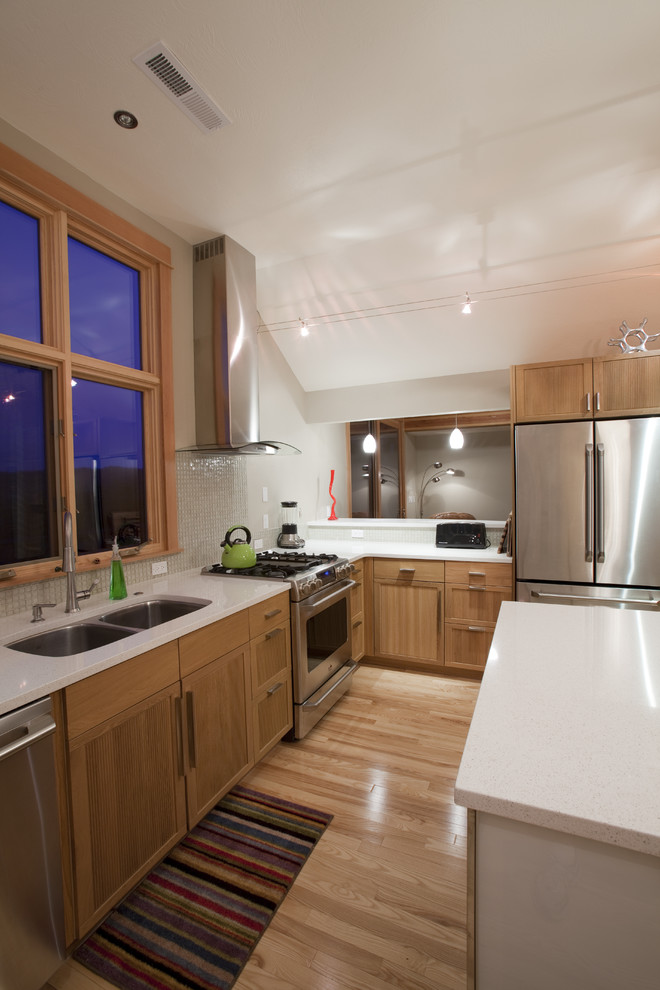 Cette photo montre une cuisine tendance en L et bois brun avec un électroménager en acier inoxydable, un évier 2 bacs, un placard avec porte à panneau encastré, une crédence blanche et une crédence en mosaïque.