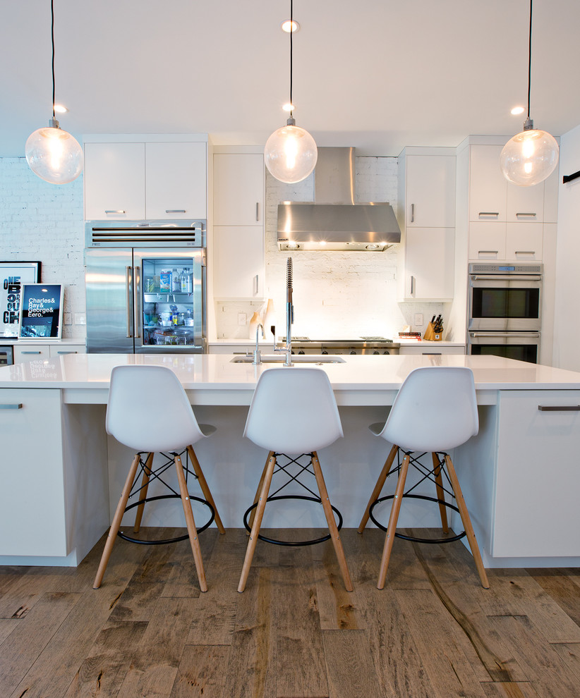 Inspiration for a medium sized contemporary galley kitchen in Orlando with a submerged sink, flat-panel cabinets, white cabinets, white splashback, stainless steel appliances, medium hardwood flooring, an island and brick splashback.