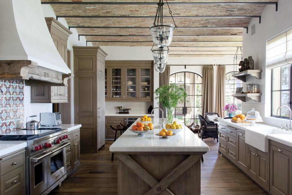 Medelhavsstil inredning av ett vit vitt kök, med en rustik diskho, luckor med upphöjd panel, flerfärgad stänkskydd, rostfria vitvaror, en köksö, brunt golv, mellanmörkt trägolv och skåp i mörkt trä