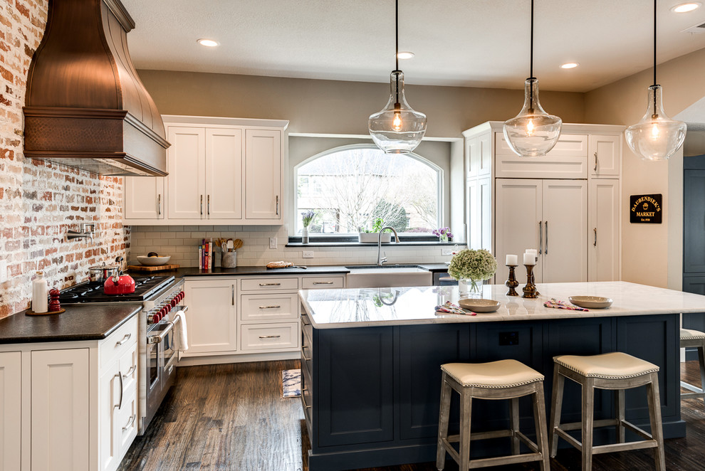 Example of a mid-sized country l-shaped medium tone wood floor and brown floor open concept kitchen design in Dallas with a farmhouse sink, shaker cabinets, white cabinets, white backsplash, subway tile backsplash, an island, marble countertops, paneled appliances and black countertops