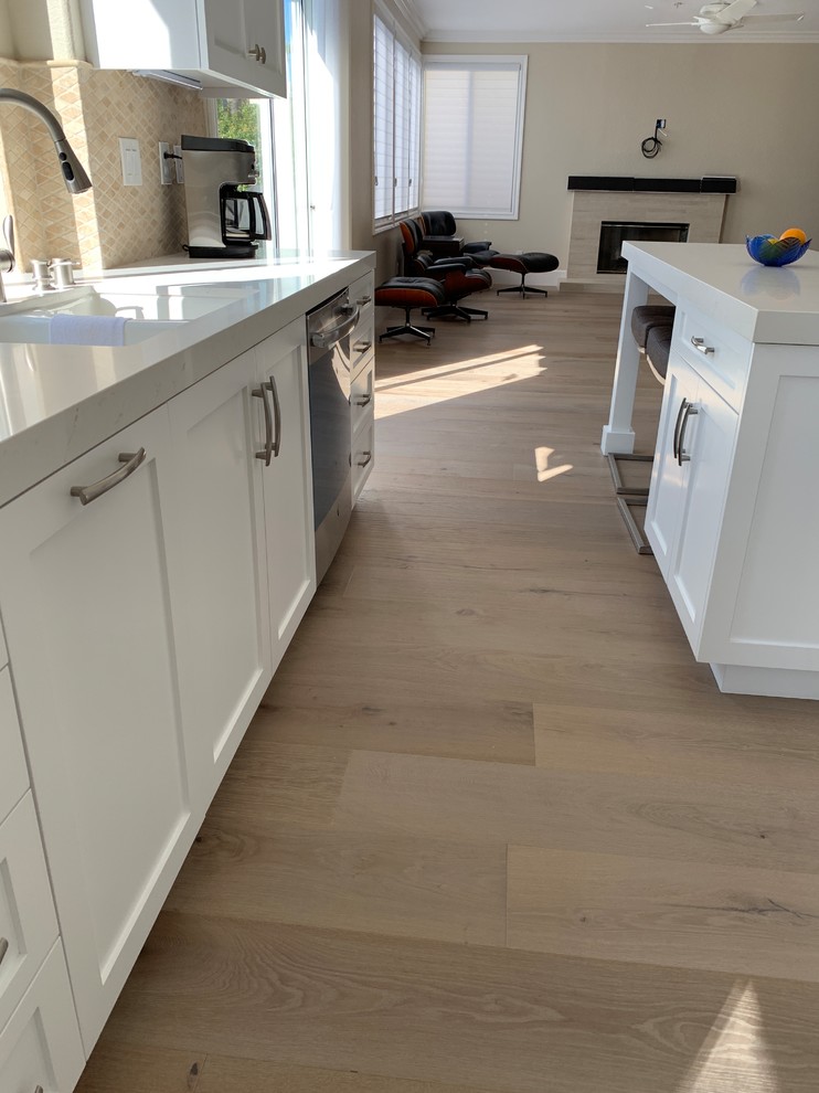 Inspiration for a medium sized classic u-shaped open plan kitchen in Orange County with a double-bowl sink, shaker cabinets, white cabinets, composite countertops, beige splashback, travertine splashback, stainless steel appliances, light hardwood flooring, an island, beige floors and white worktops.