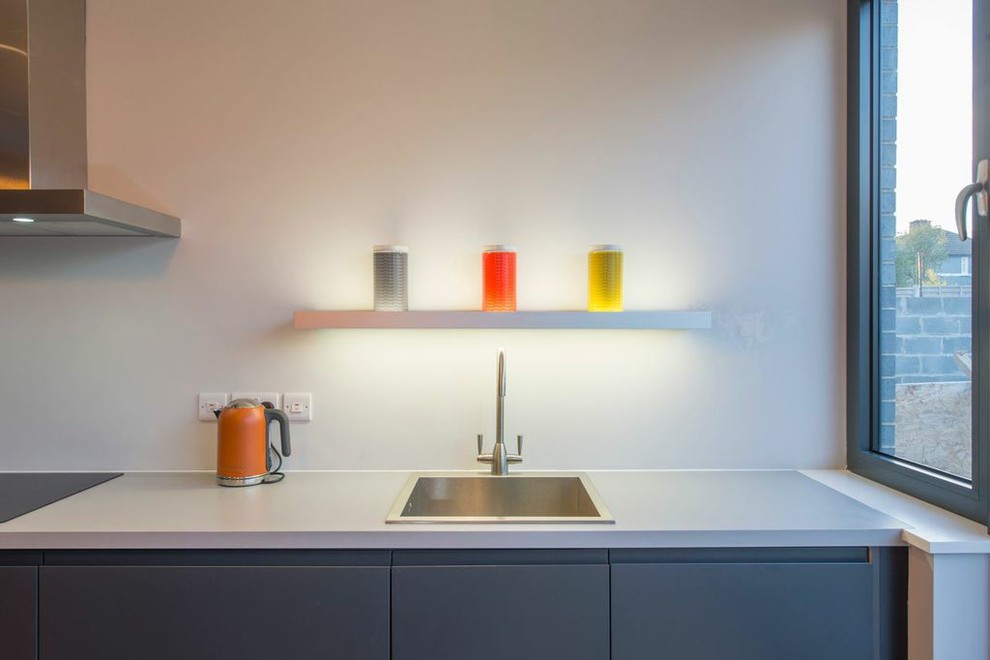 Modern inredning av ett mellanstort linjärt kök och matrum, med en integrerad diskho, släta luckor, grå skåp, laminatbänkskiva, vitt stänkskydd, integrerade vitvaror, ljust trägolv och en köksö