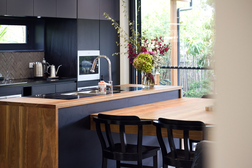 Modelo de cocina contemporánea de tamaño medio abierta con fregadero bajoencimera, armarios con paneles lisos, puertas de armario negras, encimera de madera, salpicadero gris, salpicadero de azulejos de cerámica, electrodomésticos de acero inoxidable, suelo de azulejos de cemento, una isla y suelo gris