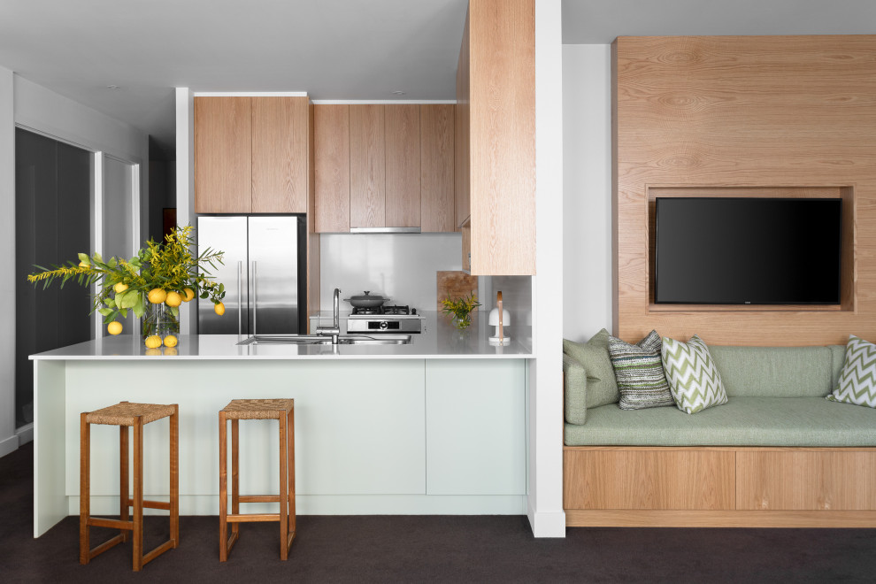 Contemporary u-shaped open plan kitchen in Melbourne with a built-in sink, flat-panel cabinets, medium wood cabinets, white splashback, stainless steel appliances, a breakfast bar, black floors and white worktops.