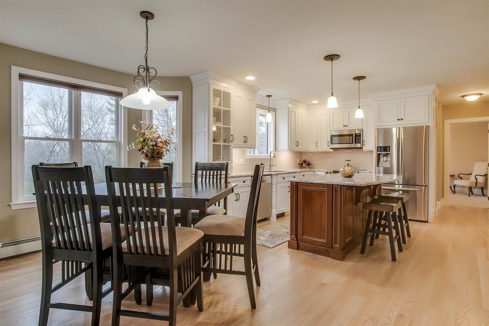 Eat-in kitchen - mid-sized traditional l-shaped light wood floor eat-in kitchen idea in Boston with a single-bowl sink, flat-panel cabinets, white cabinets, granite countertops, beige backsplash, subway tile backsplash, stainless steel appliances, an island and multicolored countertops
