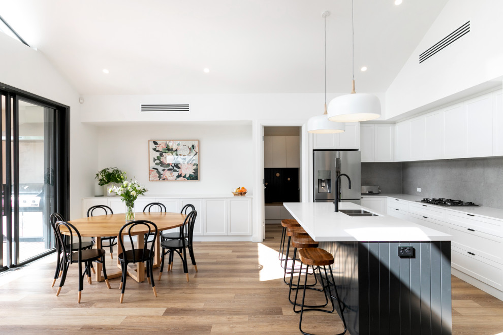 This is an example of a classic u-shaped kitchen/diner in Adelaide with a double-bowl sink, shaker cabinets, white cabinets, grey splashback, stainless steel appliances, medium hardwood flooring, an island, brown floors and white worktops.