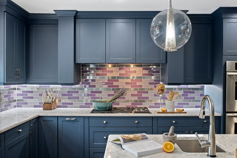 Photo of an expansive bohemian l-shaped kitchen/diner in Philadelphia with a single-bowl sink, flat-panel cabinets, blue cabinets, marble worktops, blue splashback, glass tiled splashback, stainless steel appliances, dark hardwood flooring, an island, brown floors and white worktops.