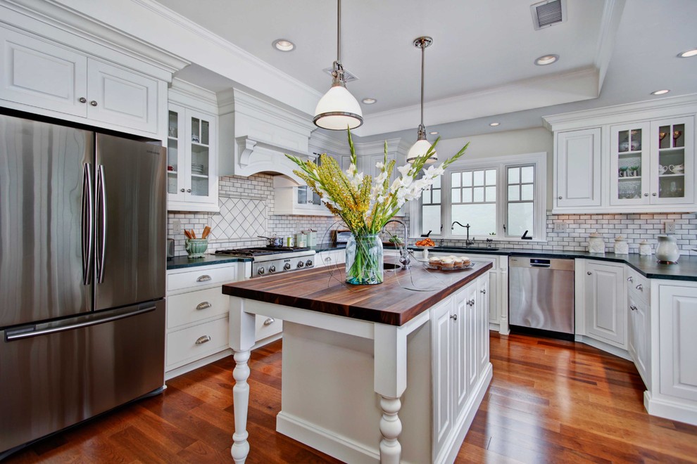 Example of a beach style kitchen design in San Diego with stainless steel appliances, wood countertops, flat-panel cabinets, white cabinets and white backsplash