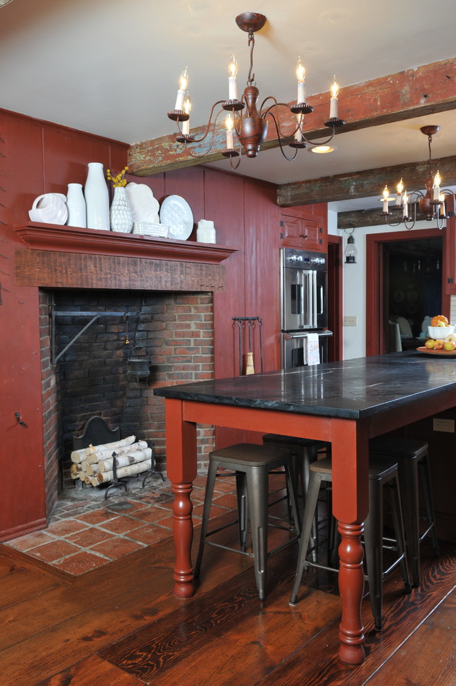 Inspiration for a mid-sized rustic l-shaped medium tone wood floor and beige floor kitchen remodel in Orange County with a farmhouse sink, raised-panel cabinets, red cabinets, soapstone countertops, beige backsplash, subway tile backsplash, stainless steel appliances and an island