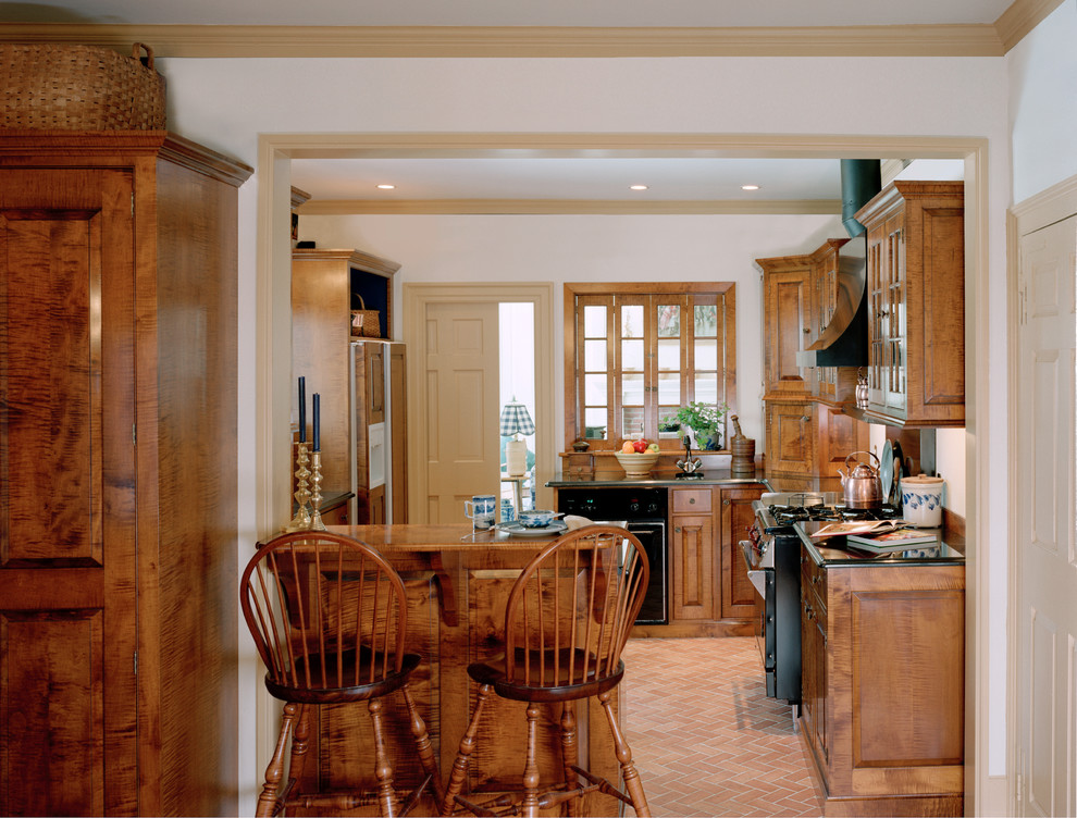 Aménagement d'une cuisine américaine classique en bois brun de taille moyenne avec un placard à porte affleurante, un plan de travail en granite, un électroménager noir, tomettes au sol et une péninsule.