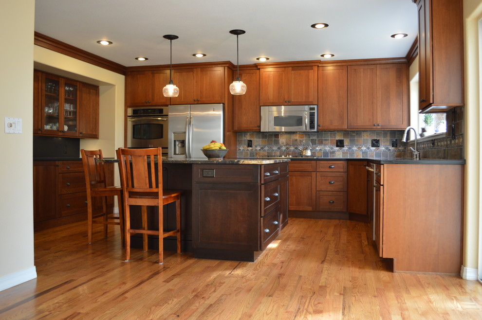 Foto de cocina de estilo americano con armarios estilo shaker, puertas de armario de madera oscura, electrodomésticos de acero inoxidable, una isla y salpicadero de pizarra