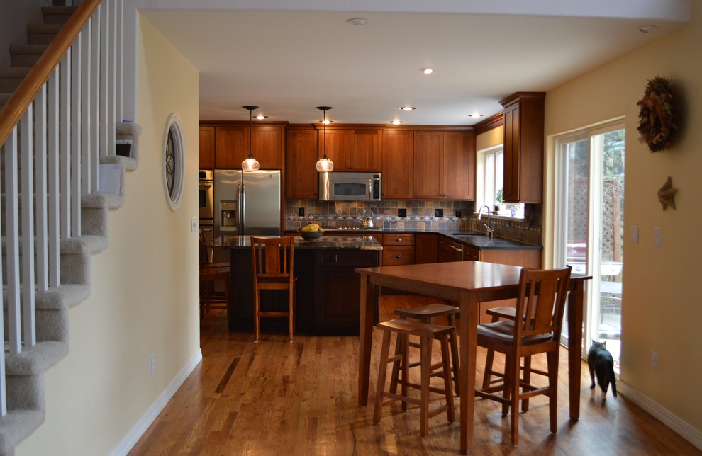 Bild på ett stort amerikanskt kök, med en undermonterad diskho, luckor med infälld panel, skåp i mellenmörkt trä, granitbänkskiva, flerfärgad stänkskydd, rostfria vitvaror, en köksö och stänkskydd i skiffer