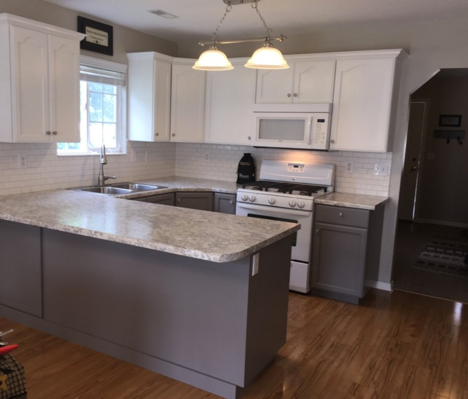 This is an example of a medium sized contemporary u-shaped kitchen/diner in Grand Rapids with a double-bowl sink, flat-panel cabinets, white cabinets, granite worktops, white splashback, metro tiled splashback, white appliances, laminate floors and a breakfast bar.