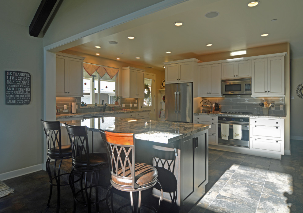 Photo of a medium sized traditional u-shaped open plan kitchen in San Luis Obispo with a single-bowl sink, shaker cabinets, grey cabinets, granite worktops, grey splashback, glass tiled splashback, stainless steel appliances, slate flooring, an island, grey floors, grey worktops and a vaulted ceiling.