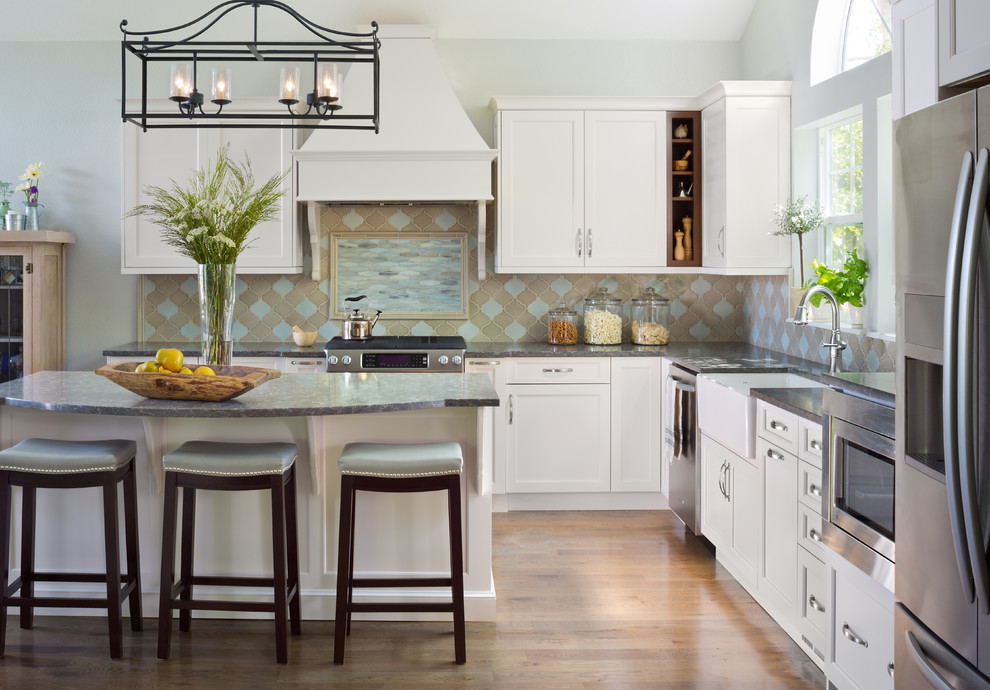 Example of a large transitional l-shaped medium tone wood floor eat-in kitchen design in Denver with a farmhouse sink, shaker cabinets, white cabinets, quartz countertops, multicolored backsplash, ceramic backsplash, stainless steel appliances and an island