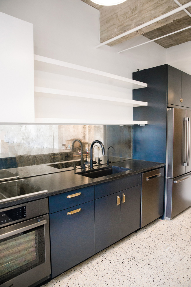 Bild på ett mellanstort industriellt svart linjärt svart kök och matrum, med en undermonterad diskho, släta luckor, blå skåp, granitbänkskiva, spegel som stänkskydd, svarta vitvaror och en köksö