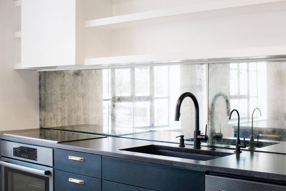 Foto di una cucina industriale di medie dimensioni con lavello sottopiano, ante lisce, ante blu, top in granito, paraspruzzi a specchio, elettrodomestici neri e top nero