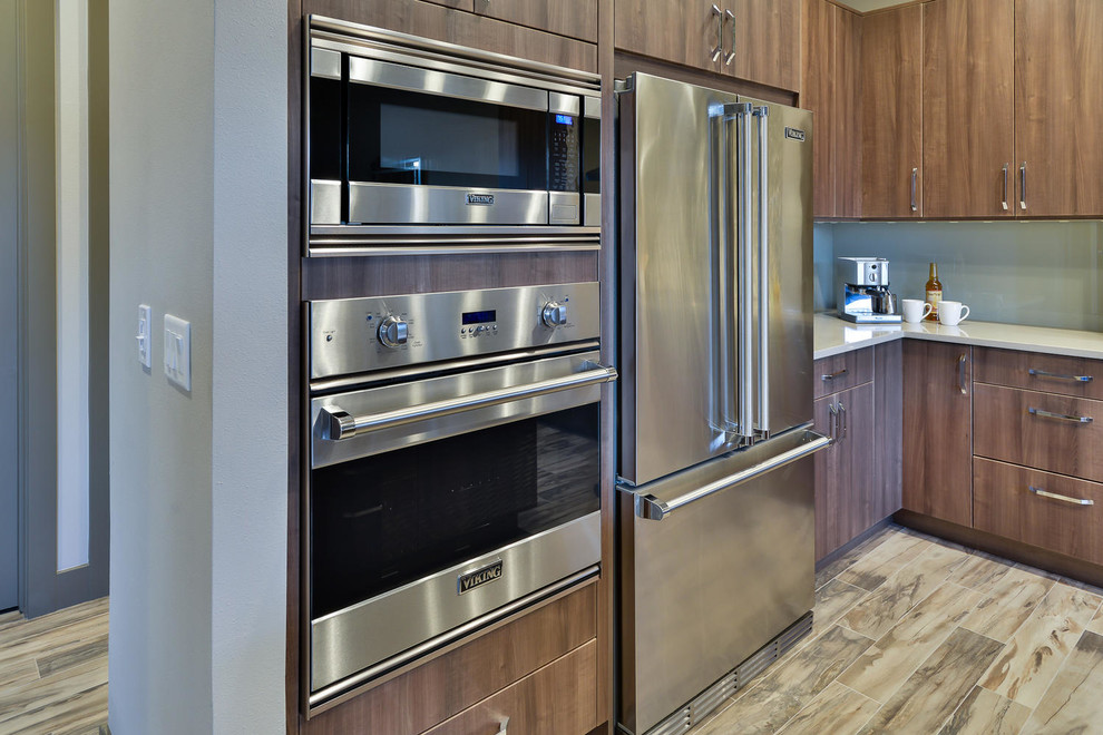 Medium sized contemporary l-shaped open plan kitchen in Denver with a submerged sink, flat-panel cabinets, medium wood cabinets, engineered stone countertops, blue splashback, glass sheet splashback, stainless steel appliances, medium hardwood flooring, an island and brown floors.