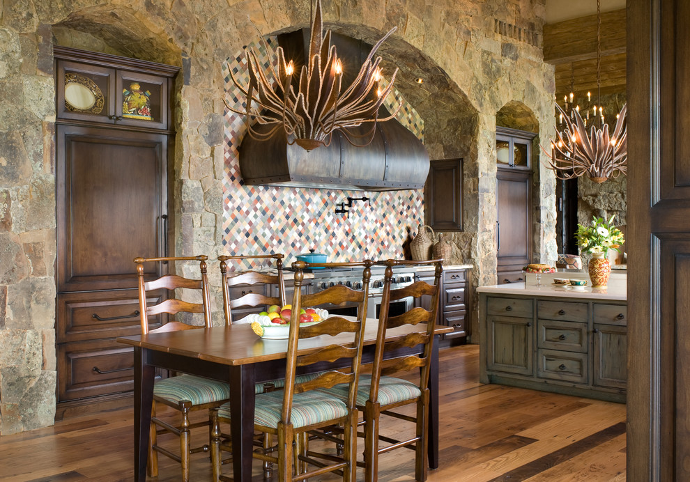 Cette image montre une cuisine américaine chalet en bois foncé avec un placard avec porte à panneau surélevé, une crédence multicolore, un électroménager en acier inoxydable, un sol en bois brun et îlot.