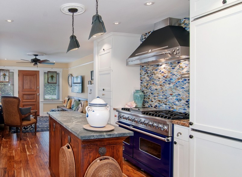 Example of a small beach style galley kitchen design in San Diego with a farmhouse sink, flat-panel cabinets, white cabinets, soapstone countertops, multicolored backsplash, glass tile backsplash, colored appliances and an island