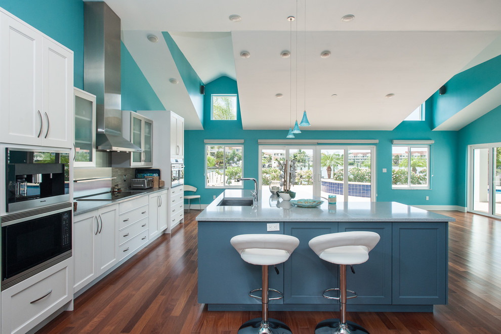 Inspiration for a large contemporary l-shaped open plan kitchen in Tampa with shaker cabinets, white cabinets, an island, a submerged sink, grey splashback, stone tiled splashback, stainless steel appliances, medium hardwood flooring and brown floors.